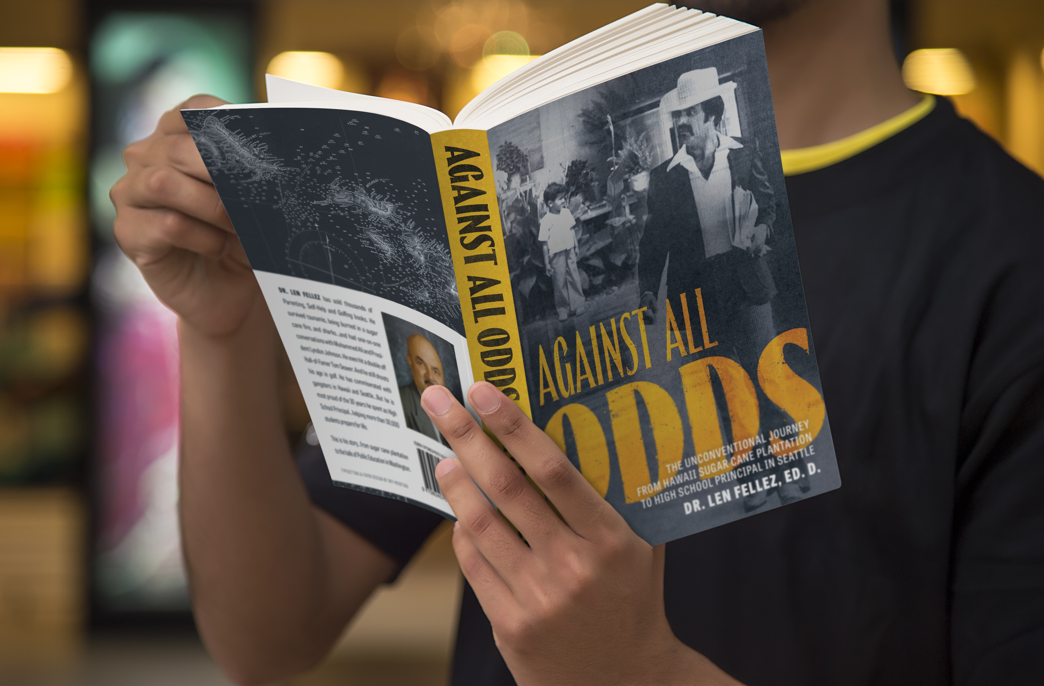 A mockup image of a softcover book titled ’Against All Odds’. The cover shows a man walking down a school hallway juxtaposed with the same man as a small child years ago. The back cover shows a map of Hawaii and a blurb.