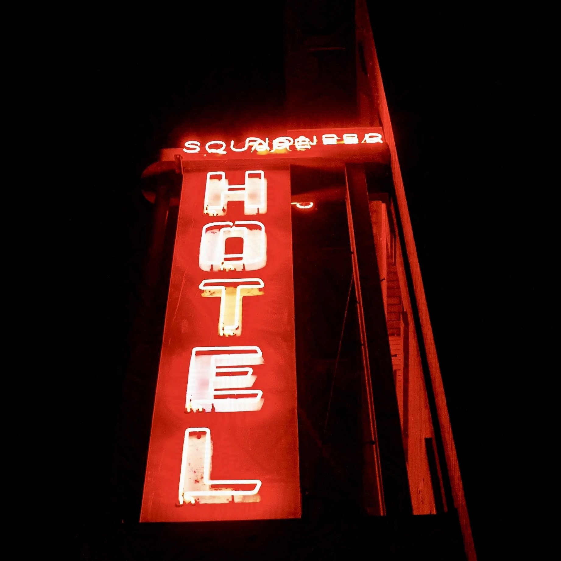 A photograph of a red neon hotel sign against darkness.